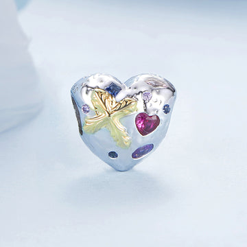 Heart-shaped silver charm with floral design and embedded gemstones on a light blue background