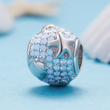 Silver charm with blue gemstones on a light blue background