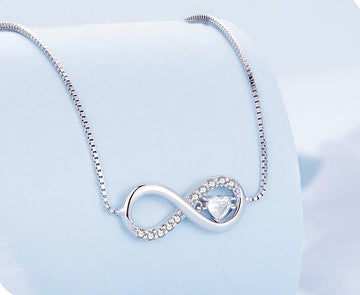 Silver infinity necklace with a heart pendant on a light blue background