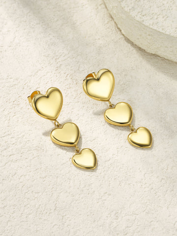 Gold heart-shaped earrings on a textured beige surface