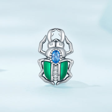 Silver beetle-shaped pendant with green and blue gemstones on a light blue background