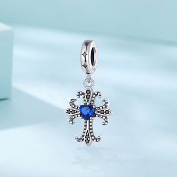 Silver cross-shaped pendant with a blue gemstone on a light blue background