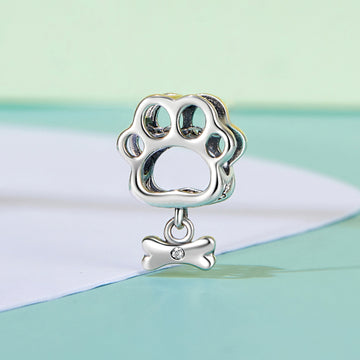 Silver paw print charm with a bone pendant on a pastel background
