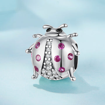Silver ladybug charm with pink gemstones on a light blue background