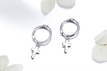 Silver hoop earrings with cross charms on a white background with flowers.