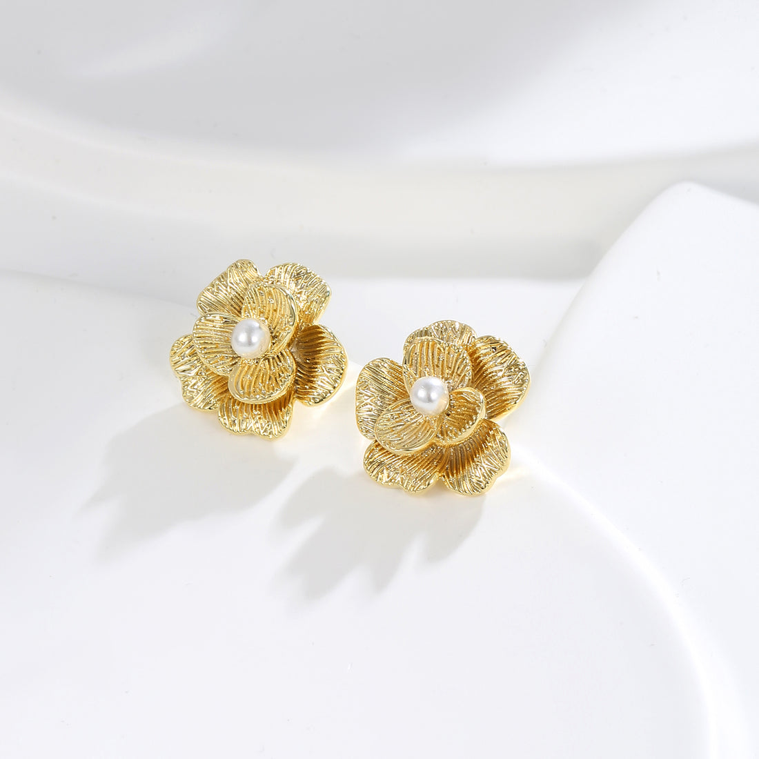 A pair of gold-colored floral stud earrings with crystal centers, displayed against a white fabric background.