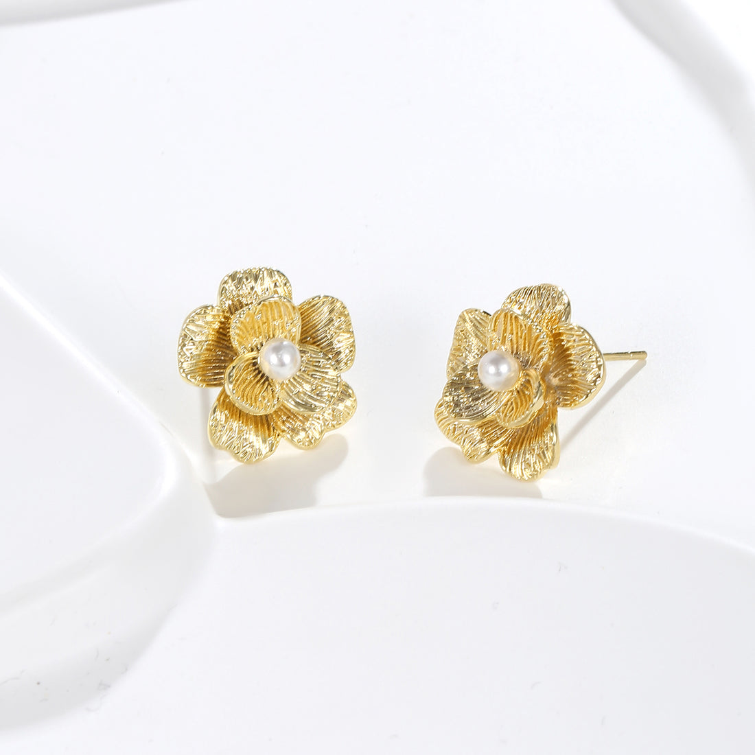 A pair of gold-colored floral stud earrings with crystal centers, displayed against a white fabric background.