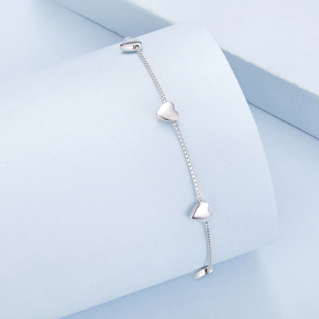 Silver bracelet with heart-shaped charms on a light blue geometric background