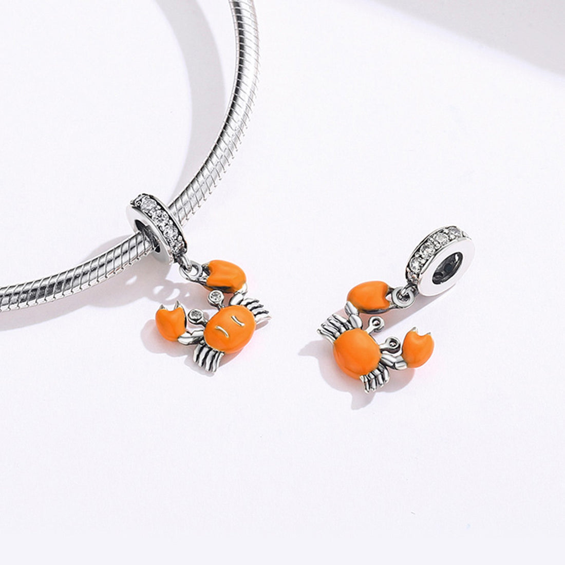 Silver charm with orange crab design on a white background