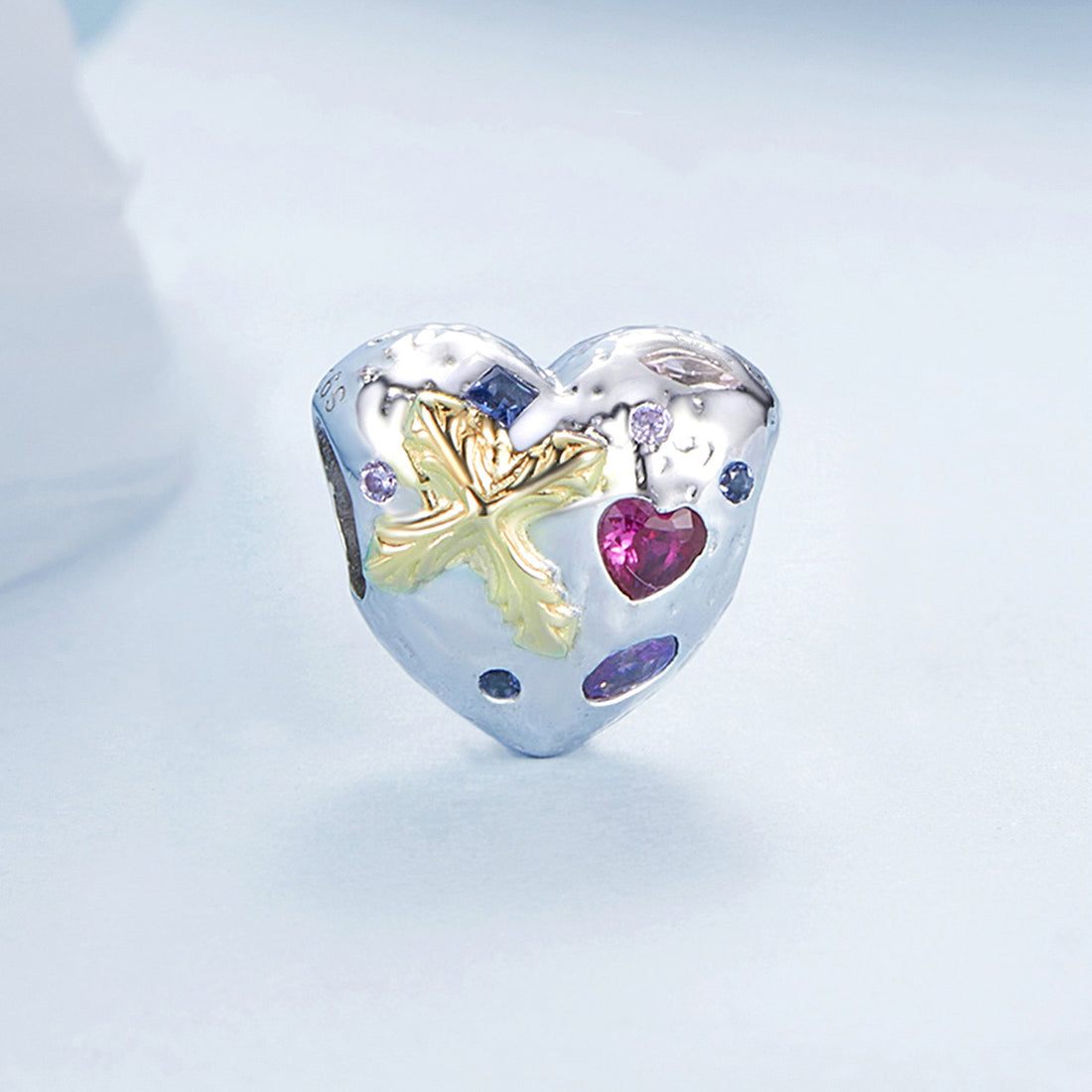 Heart-shaped silver charm with floral design and embedded gemstones on a light blue background