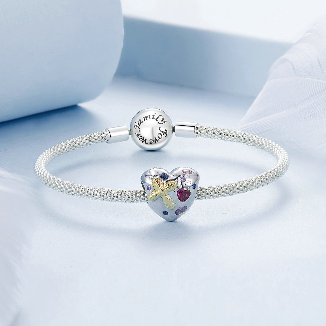 Heart-shaped silver charm with floral design and embedded gemstones on a light blue background
