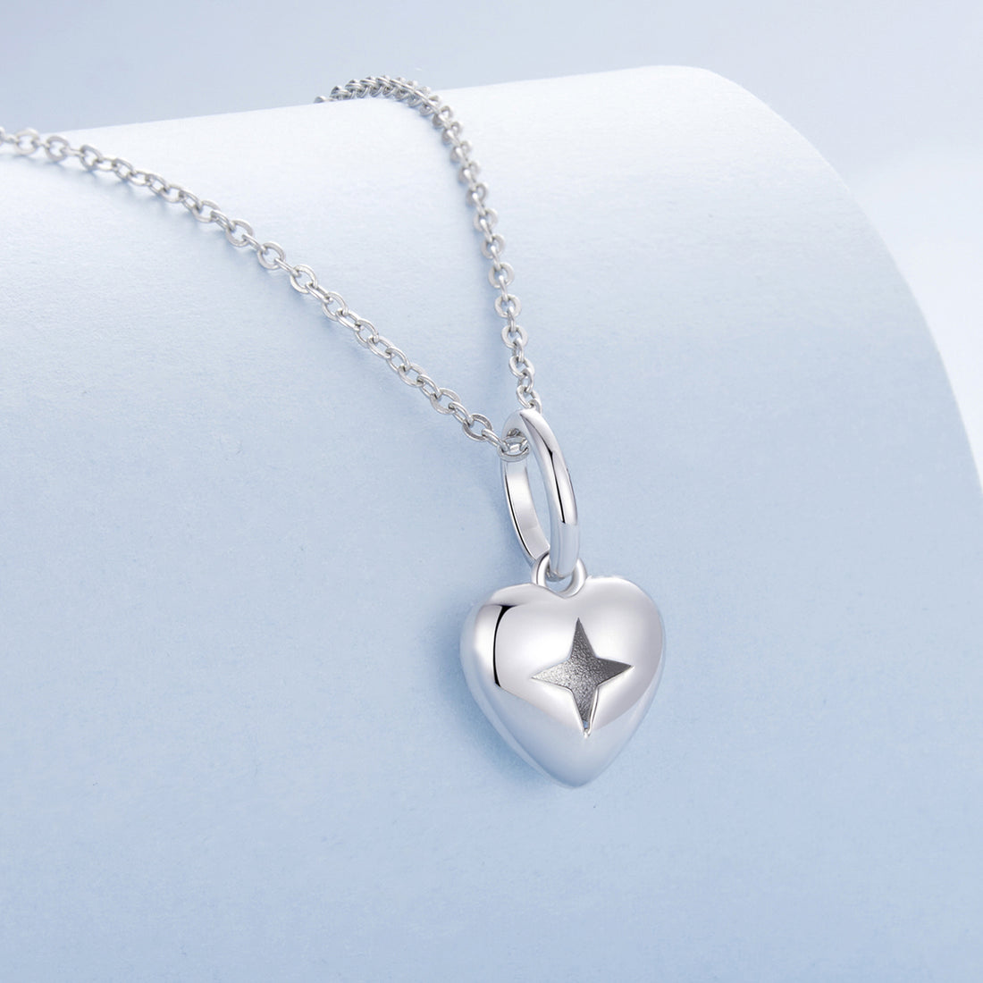 Silver heart-shaped pendant with a star engraving on a light blue background