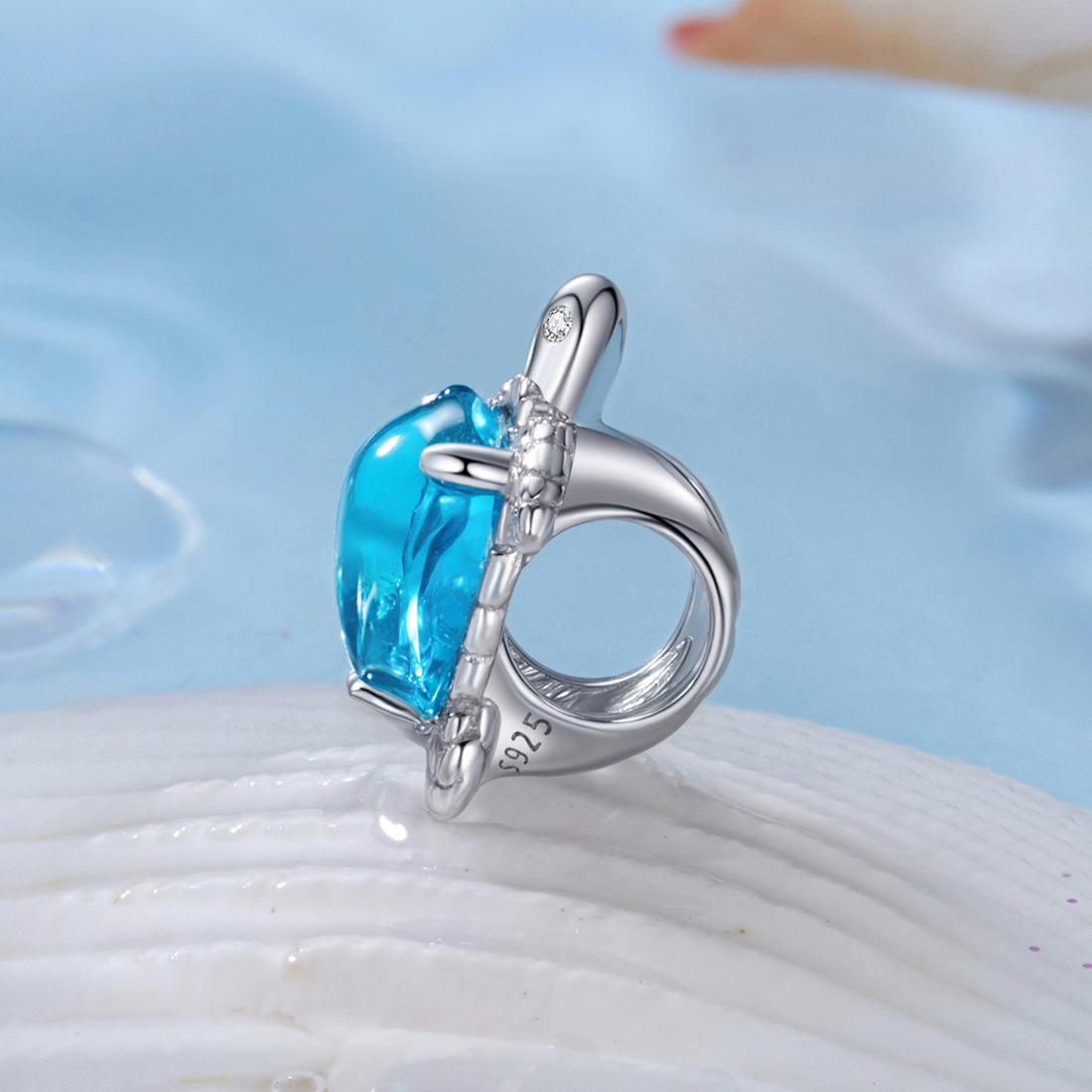 Silver turtle pendant with a blue gemstone on a beach setting