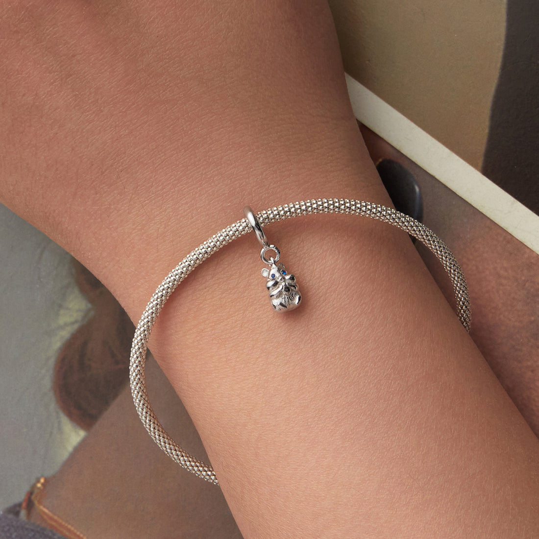 Silver bracelet with a charm on a wrist against a neutral background