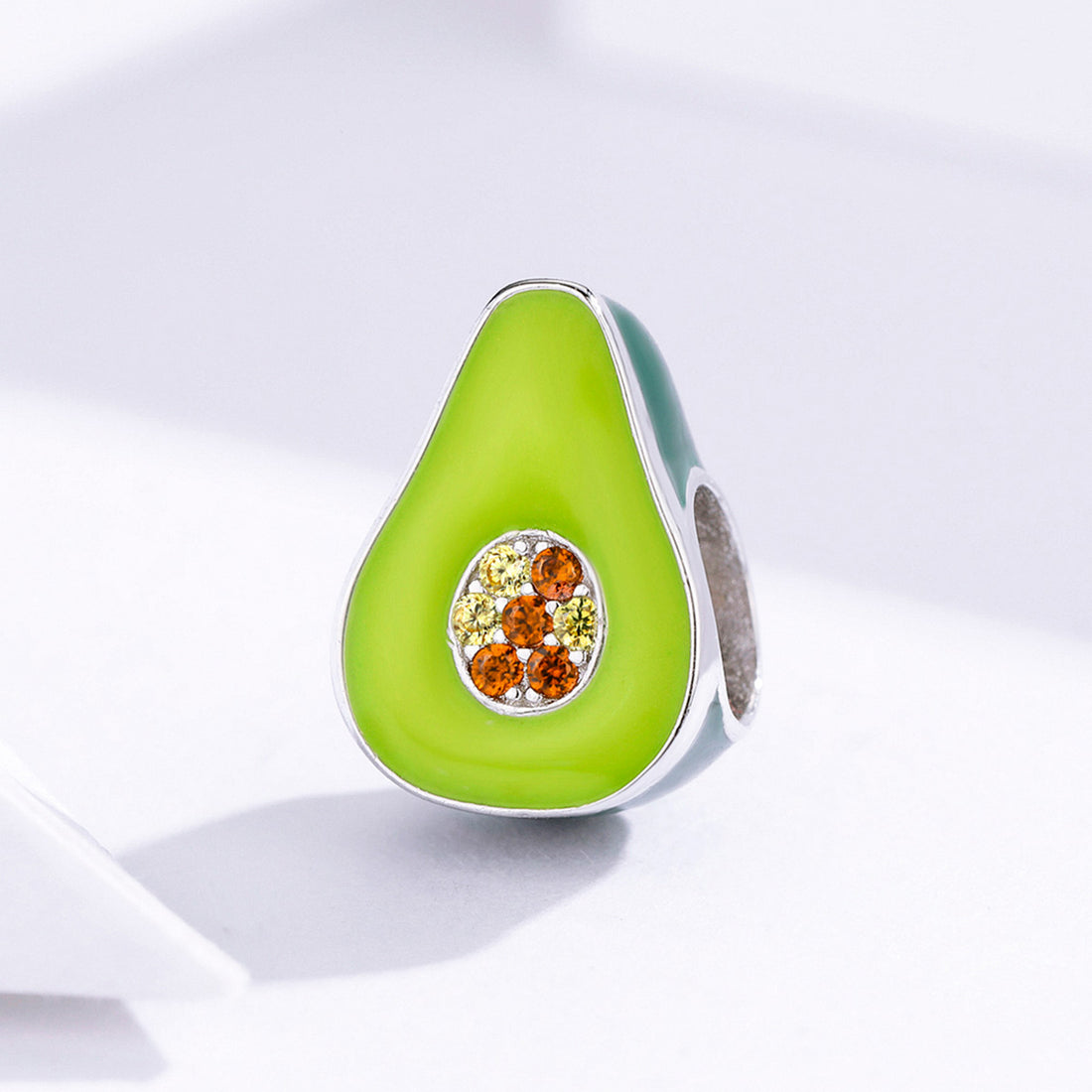 Avocado-shaped jewelry charm with gemstones on a light background
