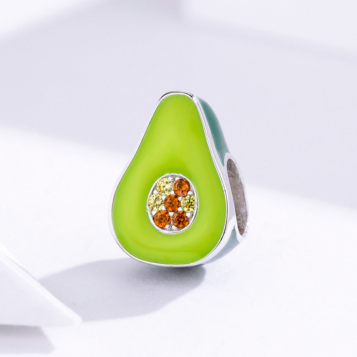 Avocado-shaped jewelry charm with gemstones on a light background