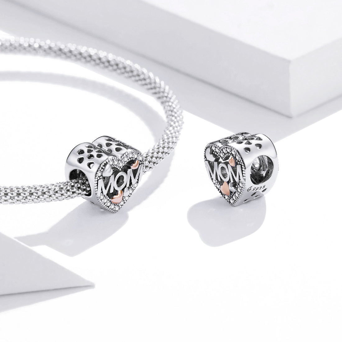 Heart-shaped silver charm with 'MOM' and heart designs on a white background