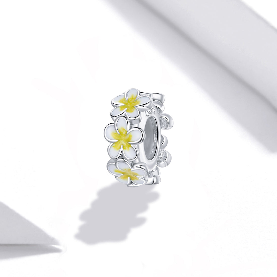 Silver ring with white and yellow flower designs on a white background