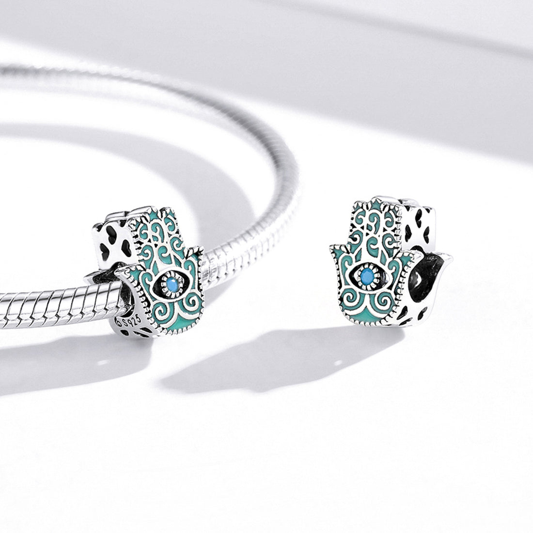 Silver and turquoise Hamsa hand charm with an eye design on a white background