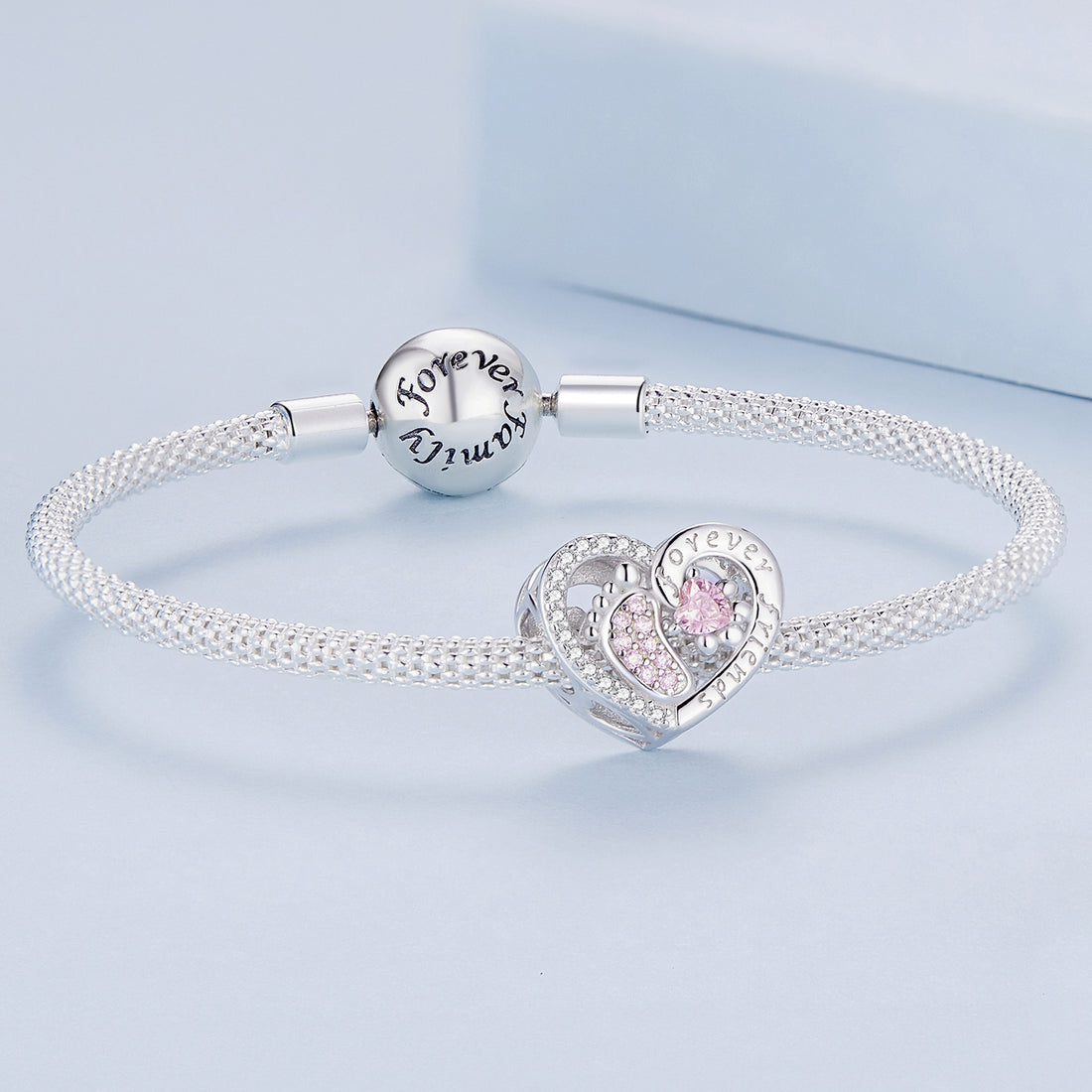 Heart-shaped silver charm with pink gemstones on a light blue background
