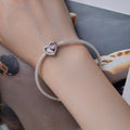 Silver bracelet with a heart-shaped charm on a wrist, blurred background