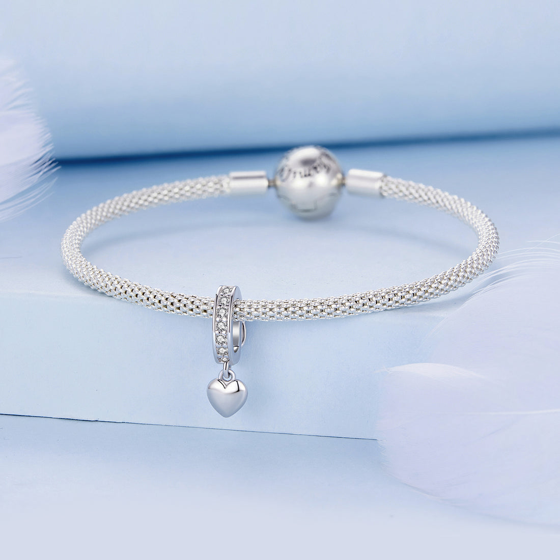 Silver charm with heart detail and clear stones on a white background