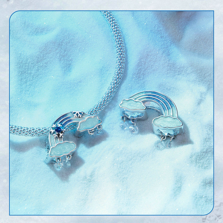 Silver necklace with cloud and rainbow pendants on a soft blue fabric background