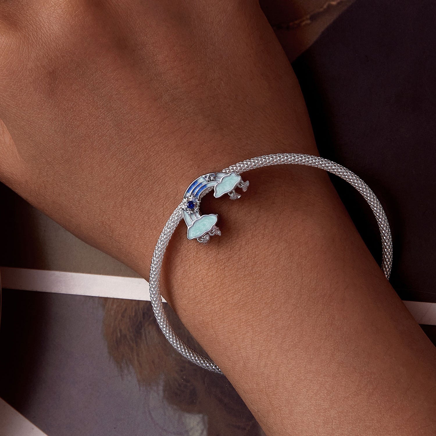 Silver bracelet with blue and green charms on a wrist against a neutral background