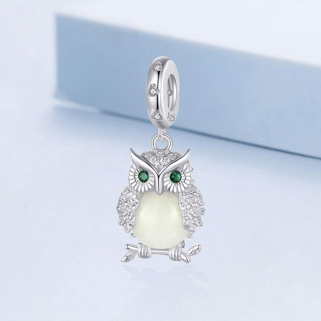 Silver owl pendant with a green gemstone on a light blue background