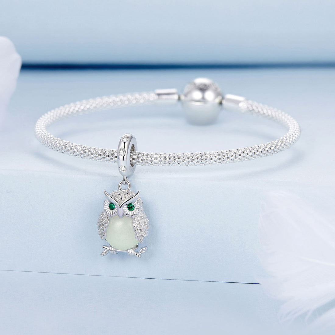 Silver owl pendant with a green gemstone on a light blue background