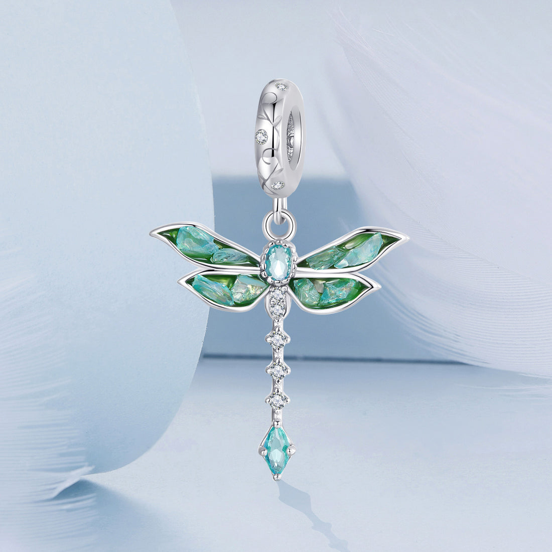 Dragonfly-shaped pendant with green and blue gemstones on a light blue background