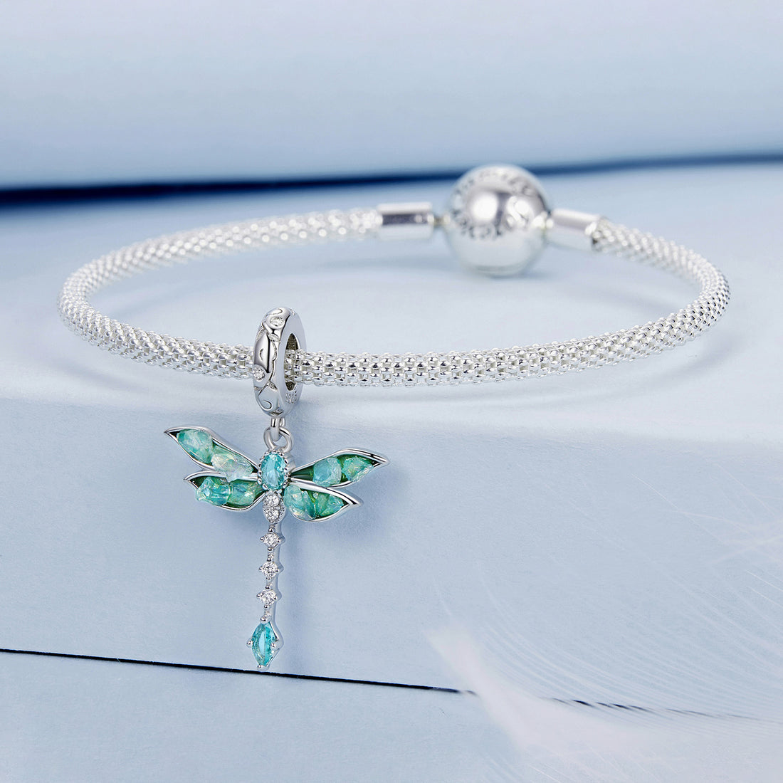 Dragonfly-shaped pendant with green and blue gemstones on a light blue background