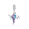 Silver bird charm with purple and blue colors on a white background