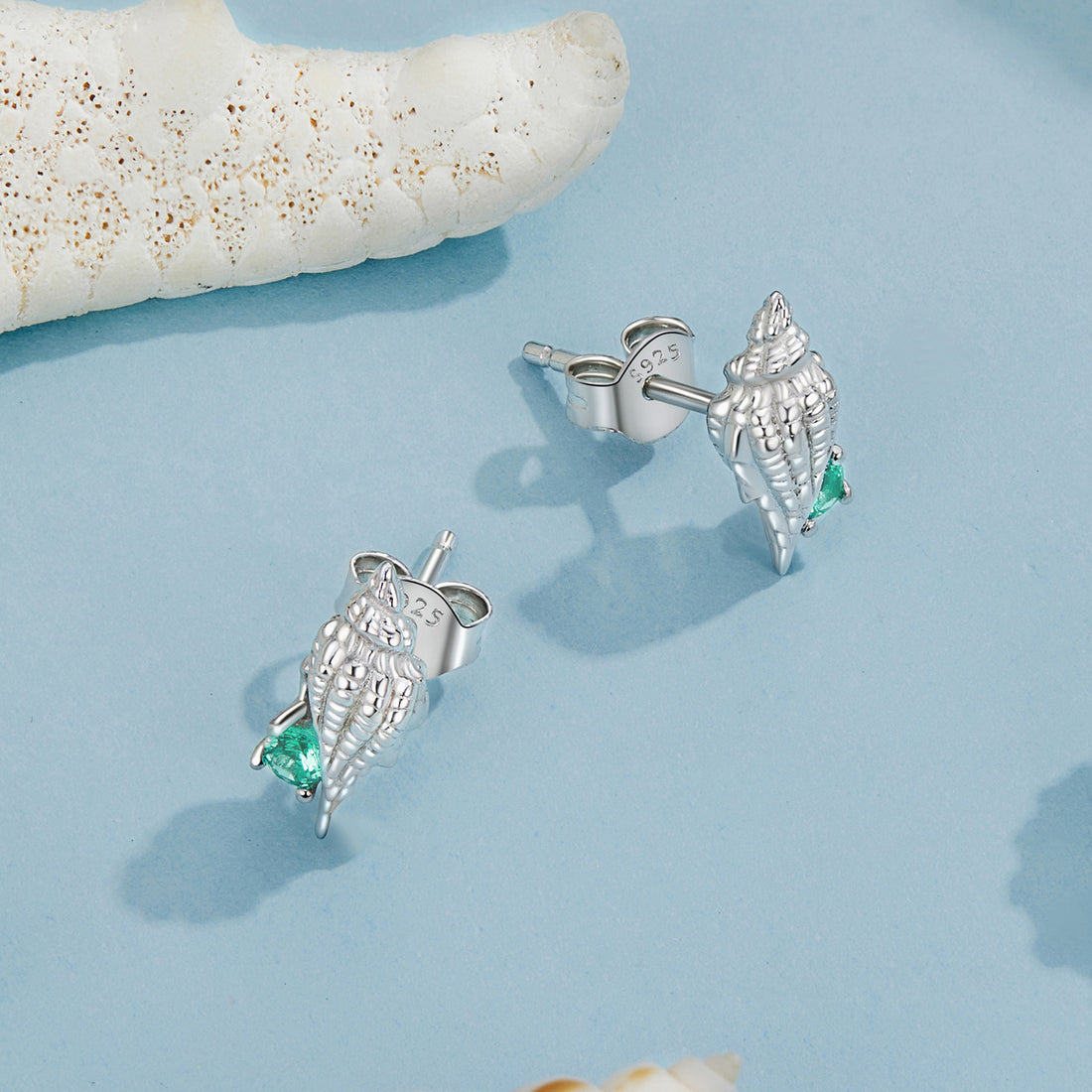 Silver shell earrings with green gemstones on a white background