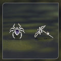Silver spider-shaped earrings with a purple gemstone on a dark green background