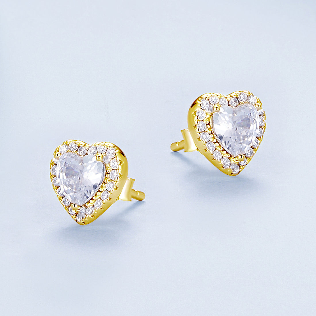 Heart-shaped earrings with clear gemstones and gold accents on a light blue background
