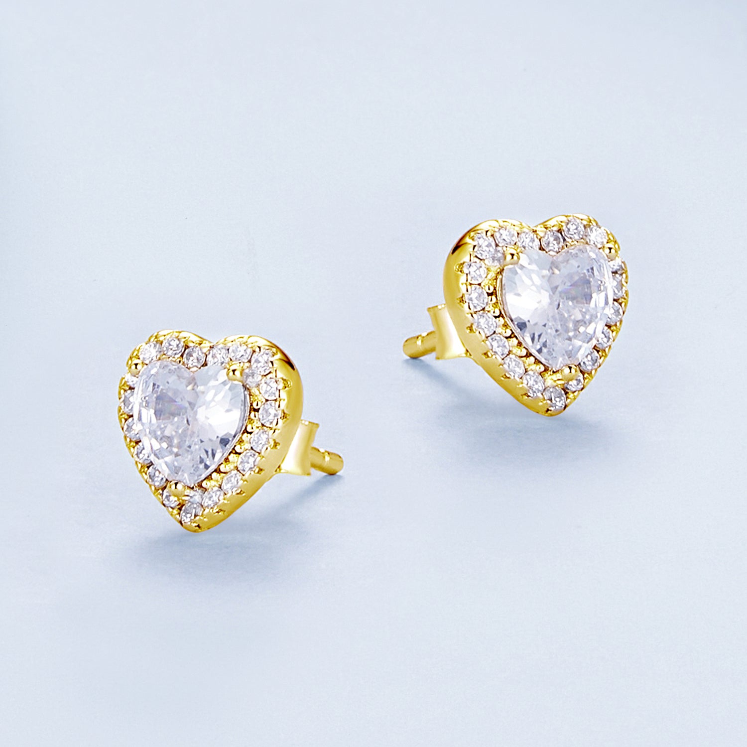 Heart-shaped earrings with clear gemstones and gold accents on a light blue background
