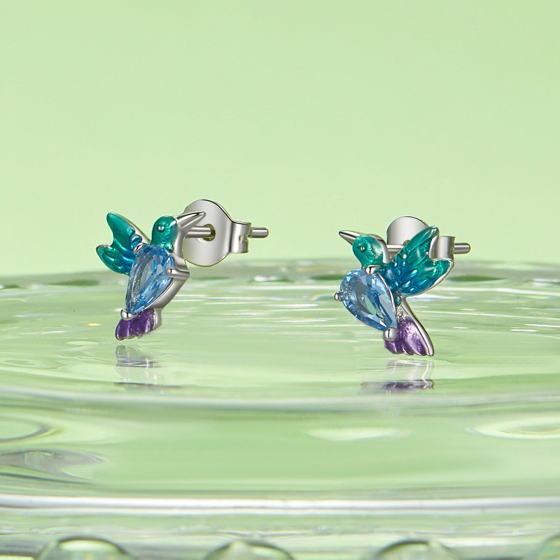 Colorful hummingbird-shaped earrings on a green background