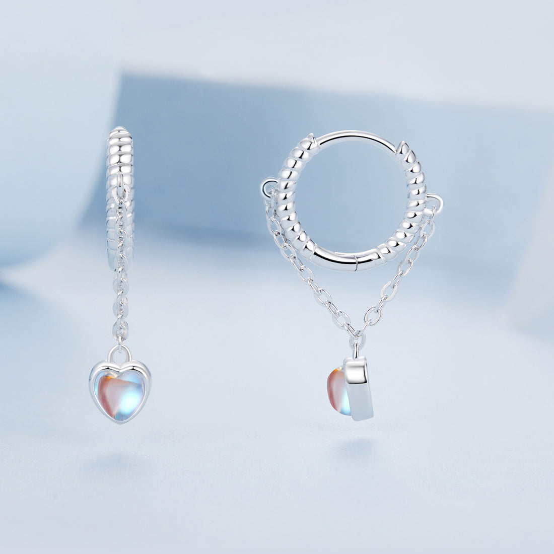 Silver hoop earrings with heart-shaped charms on a white background