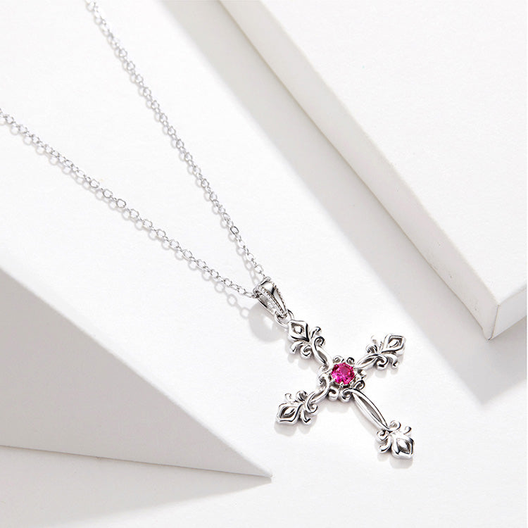 Silver cross necklace with a pink gemstone on a white background, featuring the text 'As Unique As You'.