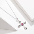 Silver cross necklace with a pink gemstone on a white background