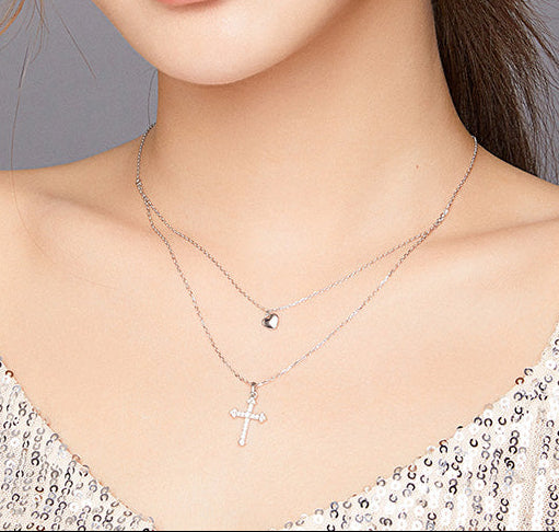 Close-up of a person wearing a silver necklace with a cross pendant, against a neutral background.