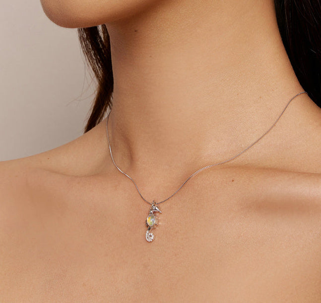 Seahorse-shaped necklace with a blue gemstone on a light blue background