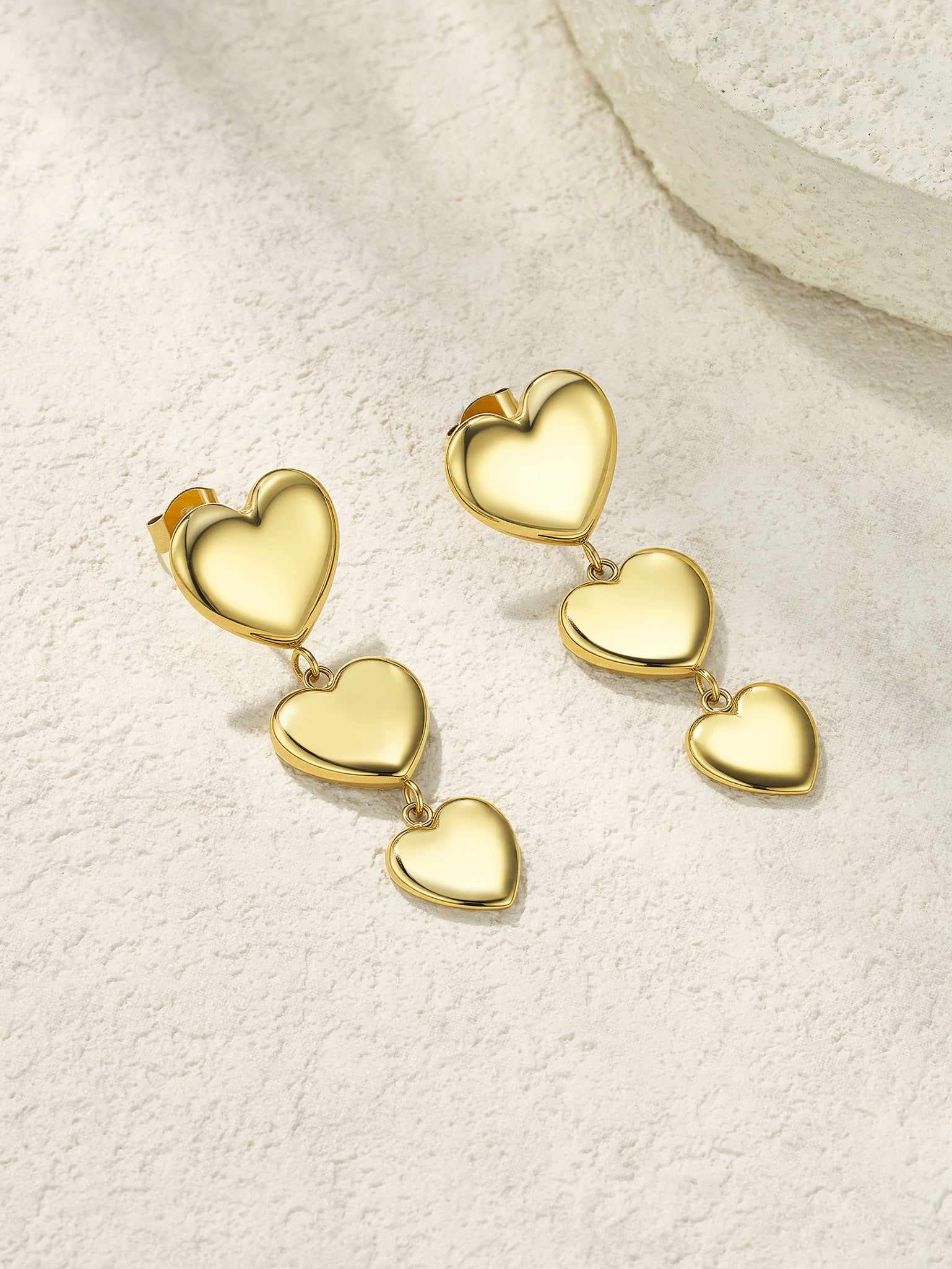Gold heart-shaped earrings on a textured beige surface