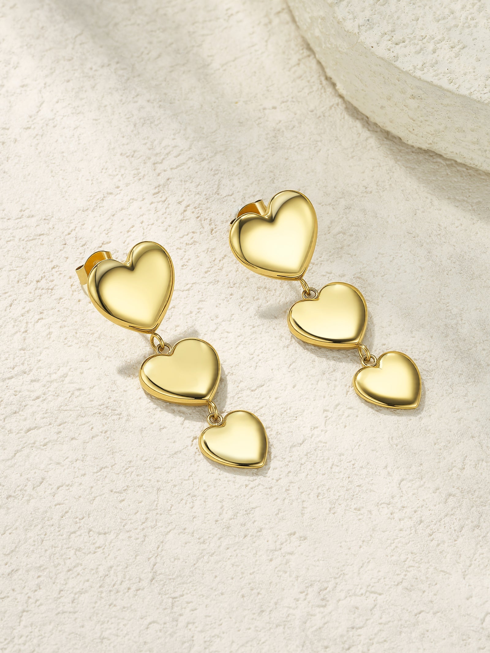 Gold heart-shaped earrings on a textured beige surface