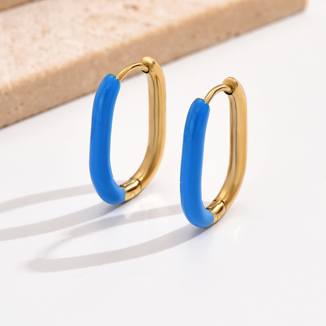 Gold hoop earrings with blue ceramic ends on a white surface