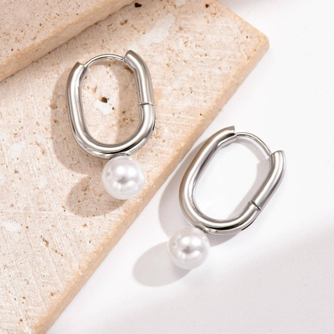 Silver hoop earrings with pearls on a textured surface