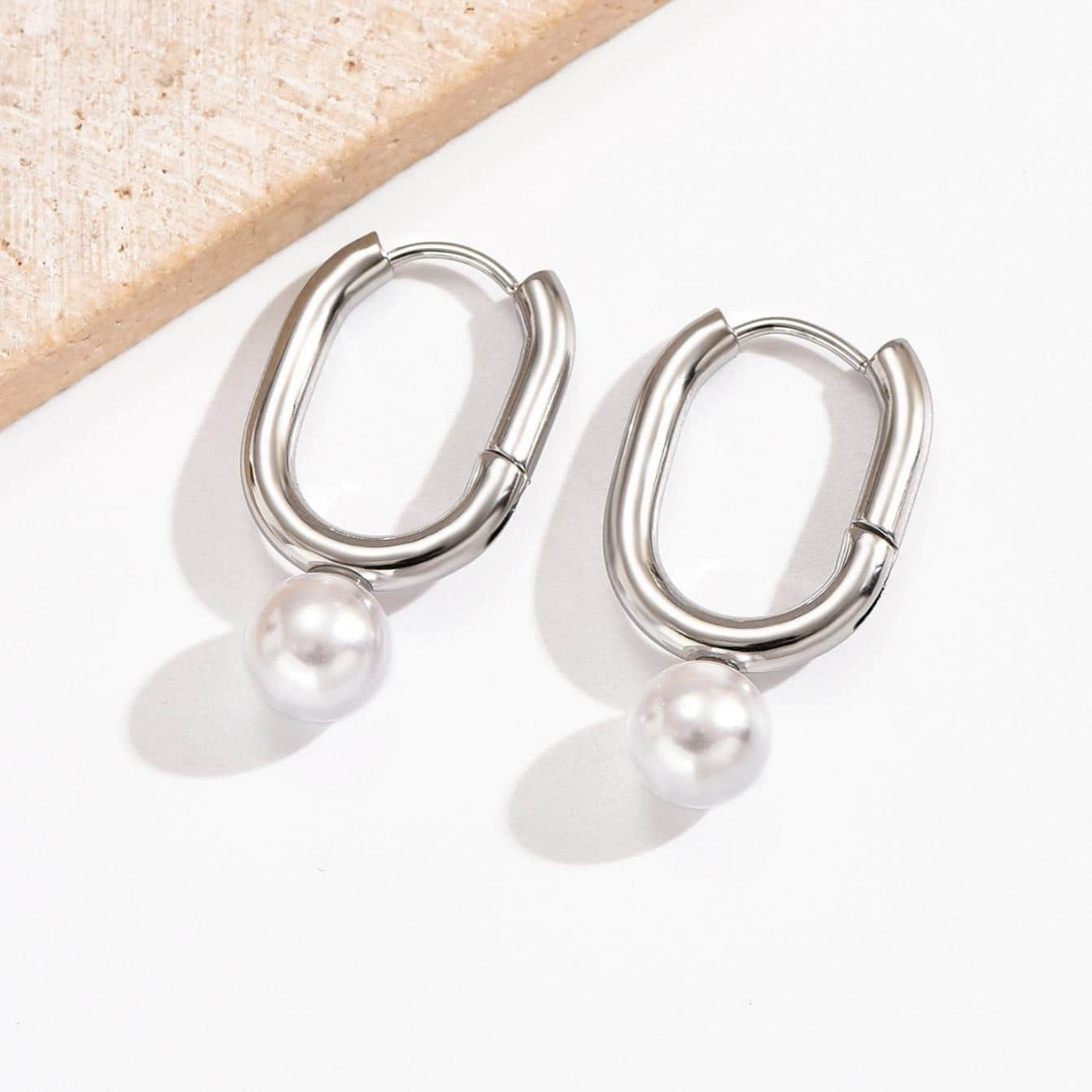 Silver hoop earrings with pearls on a textured surface
