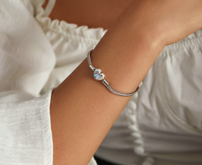 Silver bracelet with a colorful bead on a person's wrist, wearing a white outfit.