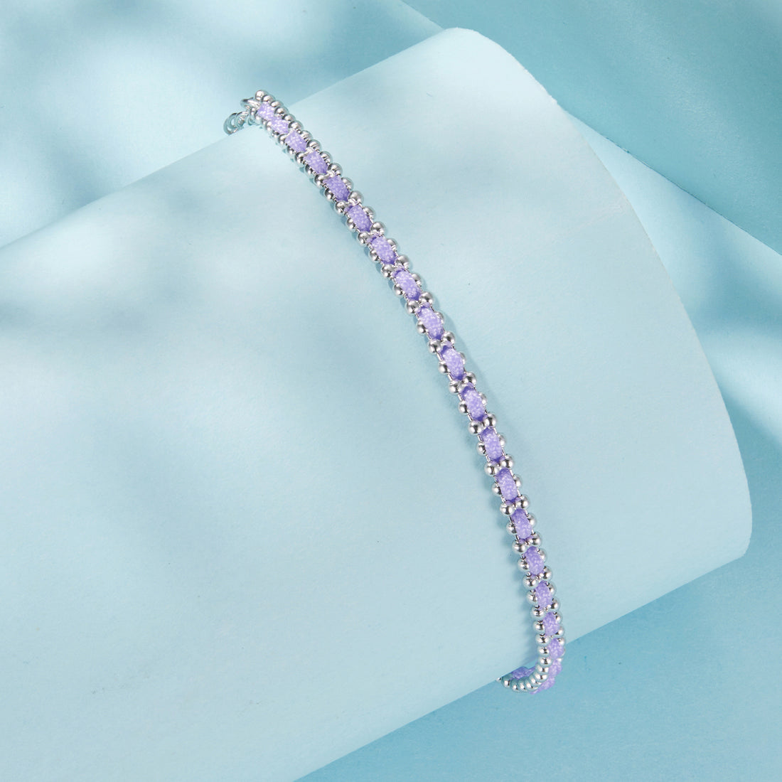 Silver bracelet with purple beads on a light blue background